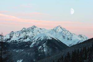 Foreground conifers Snowy mountain top in the background with Moon Eric Fisher